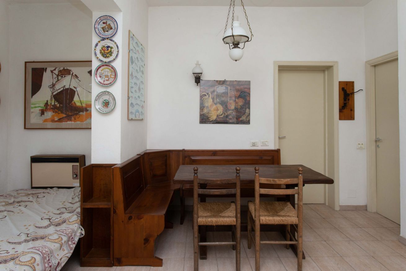 Une pièce comprenant un banc en bois, une table à manger avec des chaises, un lit et divers éléments de décoration murale, notamment des assiettes et des œuvres d’art encadrées.