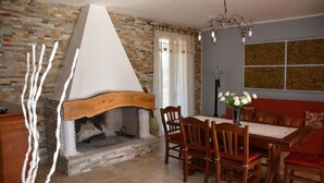 Un comedor con chimenea de ladrillo, sillas de madera, una mesa y un sofá rojo.