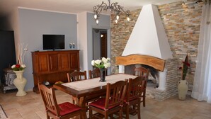 Un comedor con una mesa y sillas de madera, un televisor sobre un mueble y una chimenea con pared de piedra.
