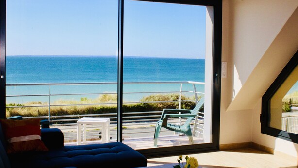 A balcony with a view of the sea, a blue sofa, and a small table. - SEAFRONT, BREATHTAKING 180°VIEW overlooking the Ocean,3 bedrooms,Private Parking (Barneville Carteret)