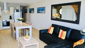 A modern living room with a black sofa, a dining table with chairs, a kitchen area with a microwave, and a large mirror on the wall. - SEAFRONT, BREATHTAKING 180°VIEW overlooking the Ocean,3 bedrooms,Private Parking (Barneville Carteret)