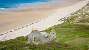 A coastal landscape with a sandy beach, a stone ruin, and a clear view of the ocean. - SEAFRONT, BREATHTAKING 180°VIEW overlooking the Ocean,3 bedrooms,Private Parking (Barneville Carteret)