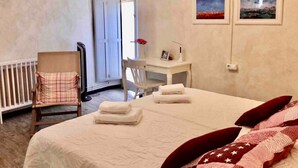 A hotel room with a bed, a desk, a chair, and a radiator.