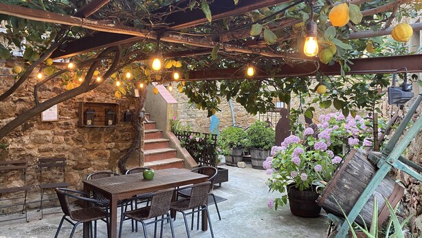 A patio area with a stone wall, wooden table and chairs, a staircase, and potted plants.