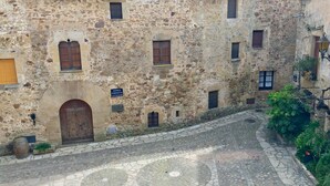 A historic stone building with a tiled roof, a central courtyard with patterned paving, and small windows.