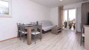 Un espace de vie compact comprenant un coin repas, un canapé et une vue sur une terrasse extérieure accessible par une porte coulissante.