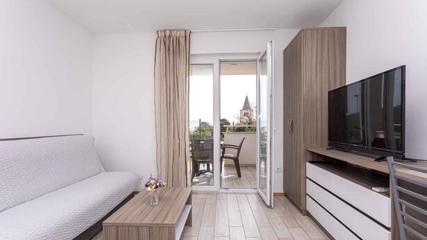 Un appartement moderne comprenant un canapé, un téléviseur, un meuble en bois et un balcon avec vue sur un immeuble.