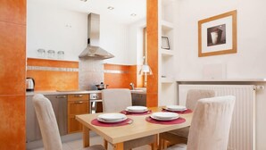 Una cocina moderna con armarios blancos, detalles en naranja y una zona de comedor con mesa de madera y sillas blancas.