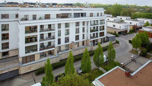 Un edificio residencial de varios pisos con balcones, un patio central y un área de estacionamiento.