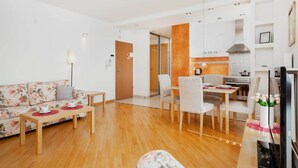 Una sala moderna con sofá, mesa de comedor y sillas, comunicada con una cocina que incluye estufa y alacenas.