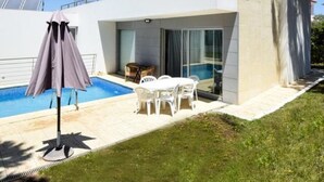 Ein modernes, zweistöckiges Haus mit Swimmingpool, Sitzgelegenheiten im Freien und einer überdachten Terrasse.