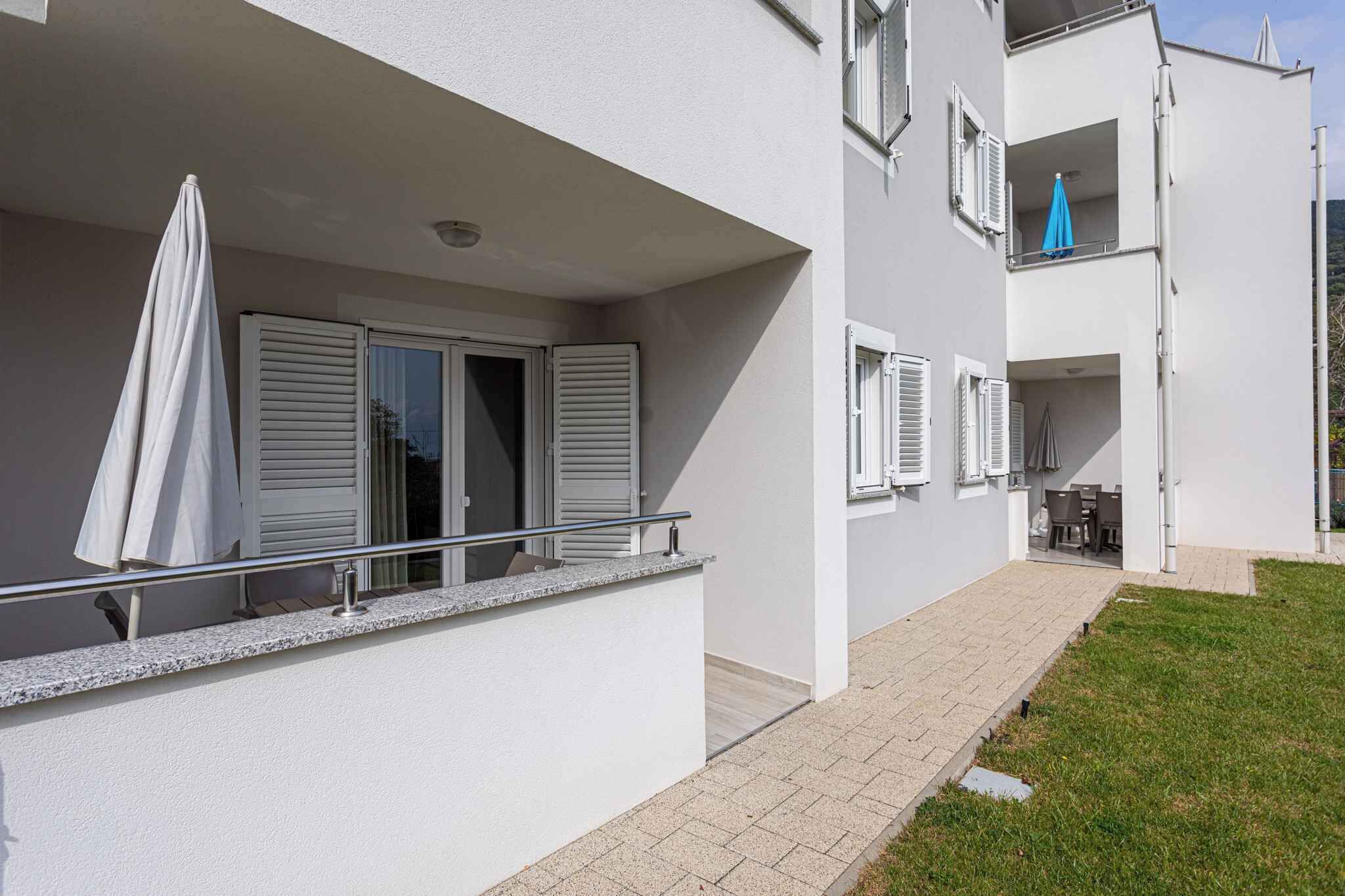 A modern apartment building with a balcony, a small outdoor seating area, and a visible window with shutters.