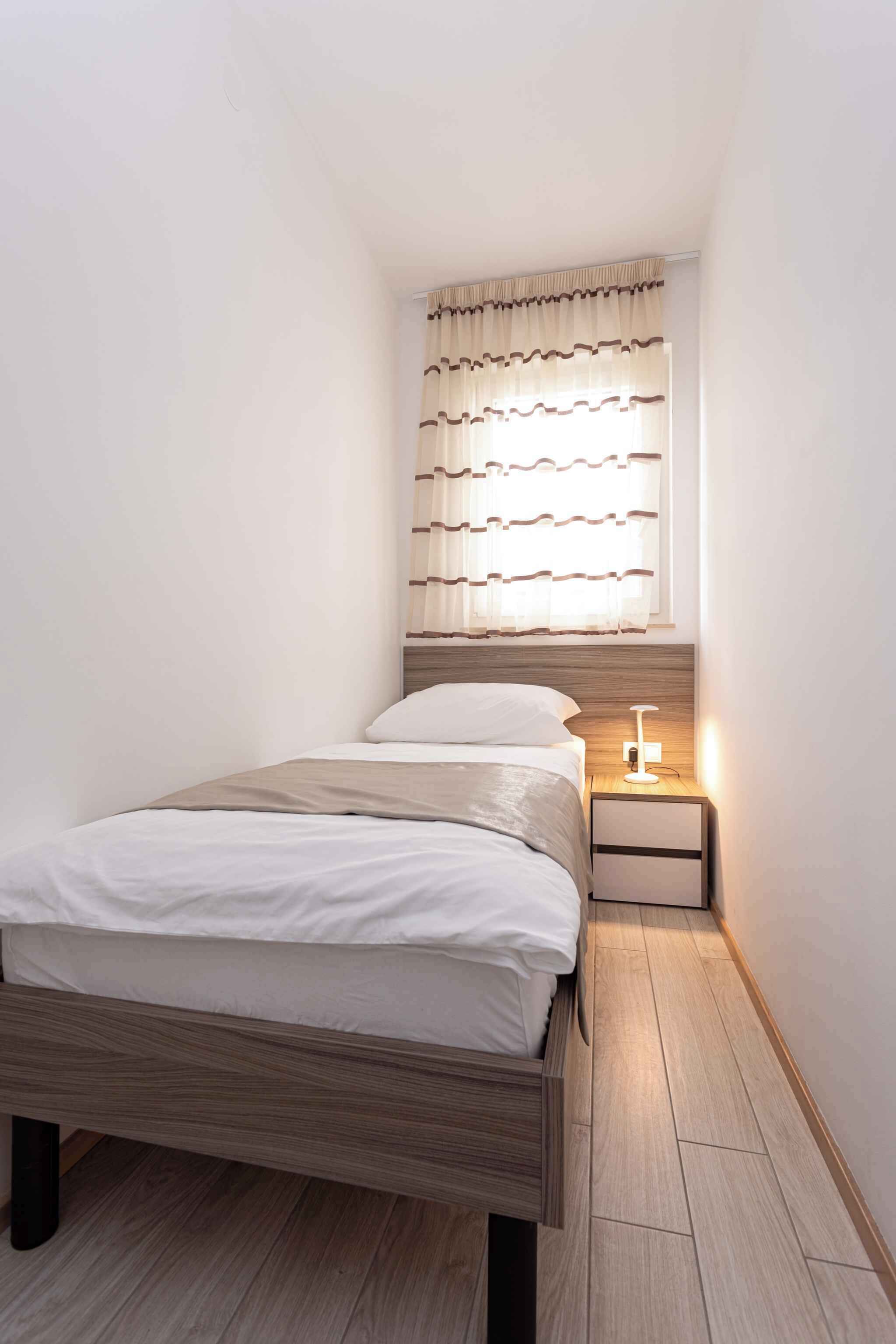 A small, neatly arranged bedroom with a single bed, a nightstand, and a window with curtains.