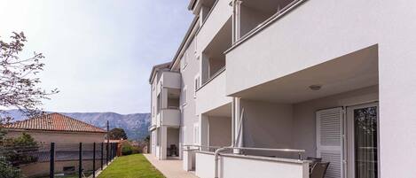 A modern apartment building with a well-maintained lawn, a fenced garden, and a balcony with outdoor furniture.