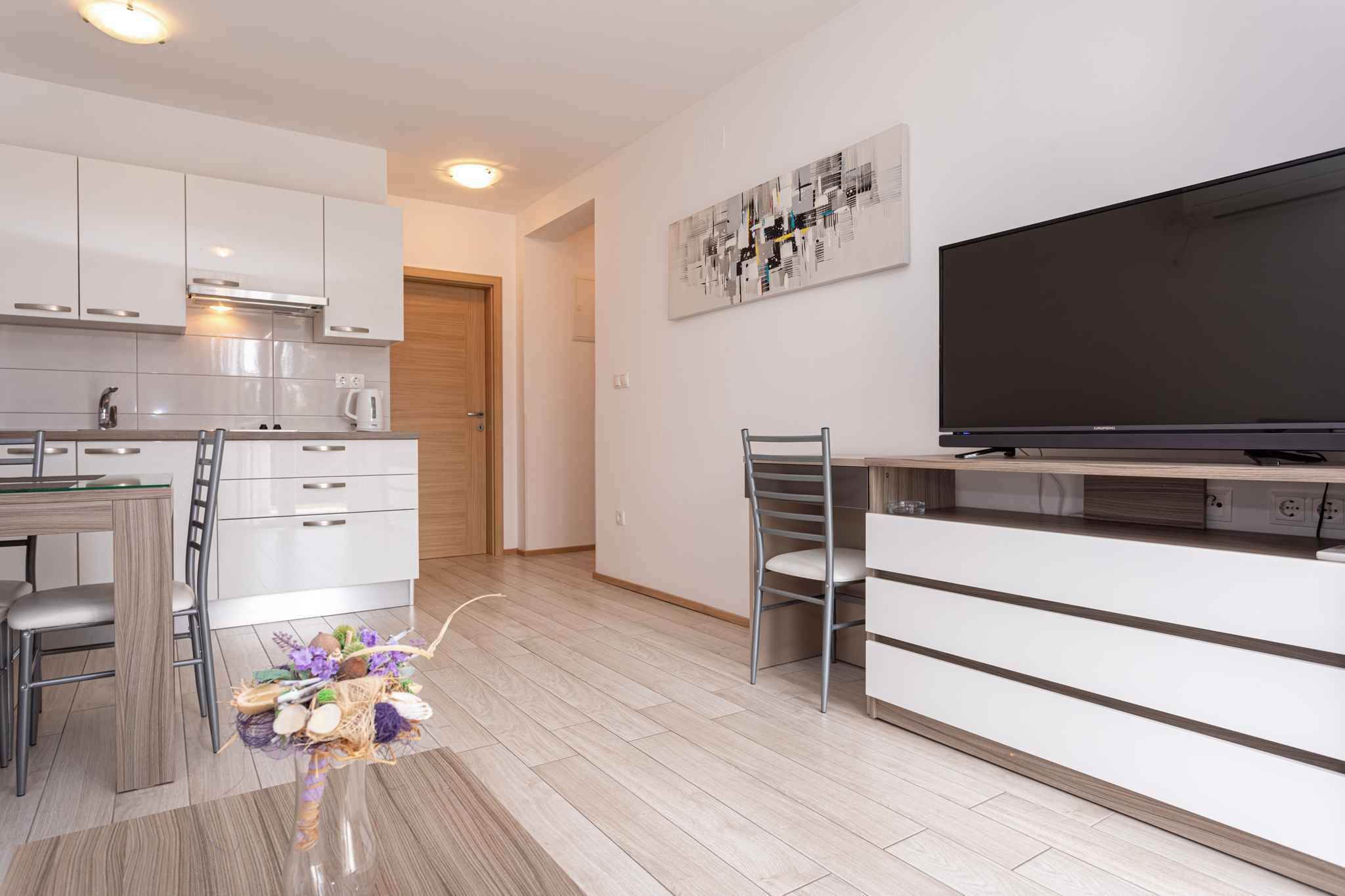 A modern kitchen with white cabinets, a dining area with a chair, a TV, and a small table.