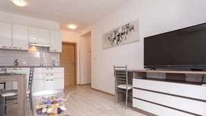 Una cocina moderna con armarios blancos, una zona de comedor con una silla, un televisor y una pequeña mesa.