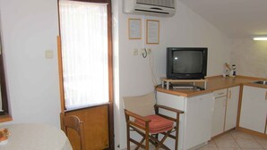 A compact kitchen with a dining area, a television, and a window with curtains.