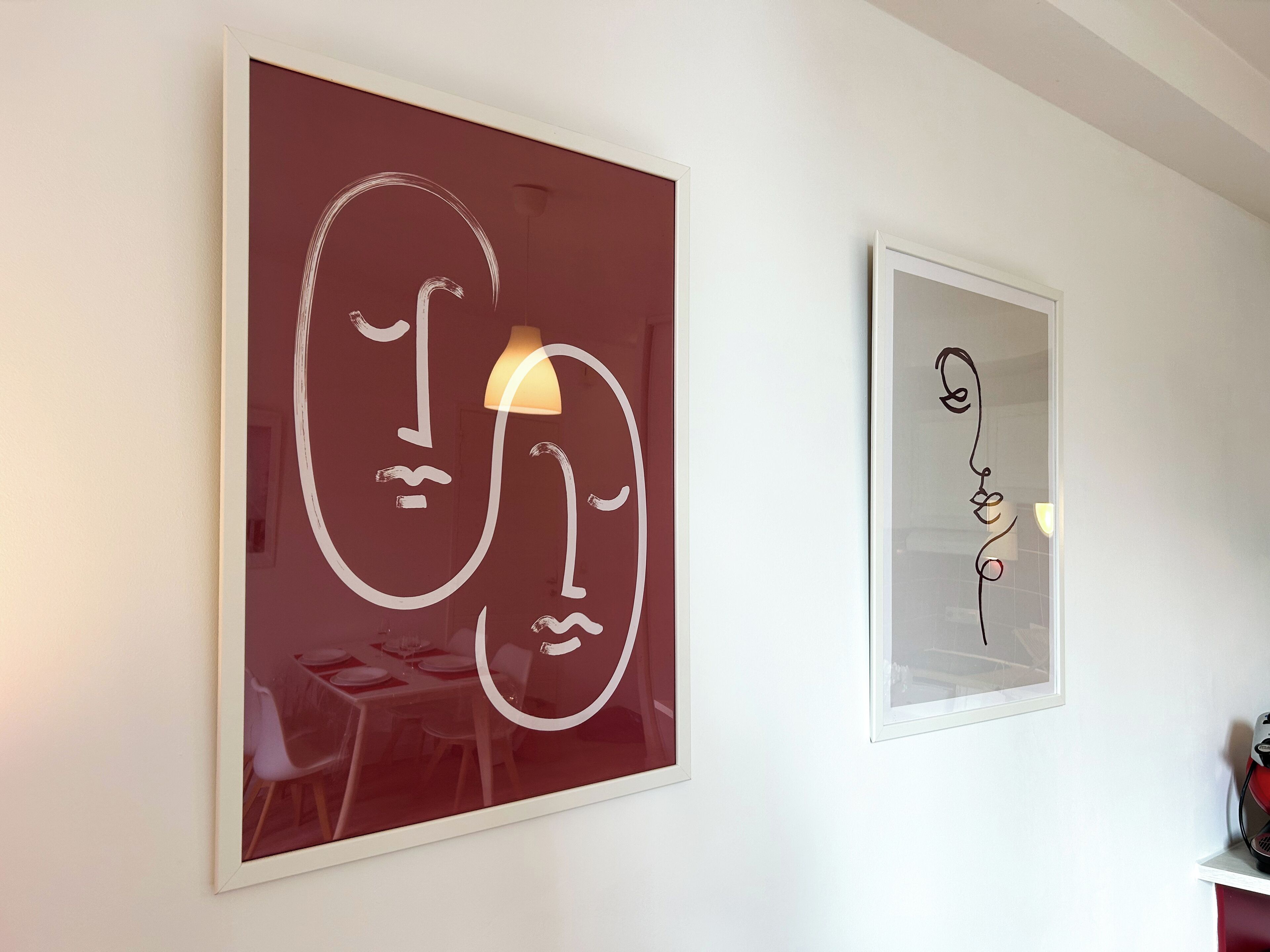 Two framed artworks on a wall, one depicting abstract faces and the other a simple line drawing.