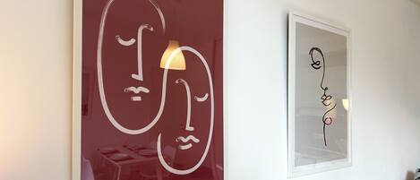 Two framed artworks on a wall, one depicting abstract faces and the other a simple line drawing.