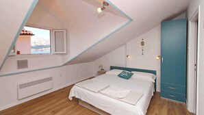 Un dormitorio con techo inclinado, una cama con ropa de cama blanca, cabecera color turquesa, un armario y una ventana con vistas a montañas.