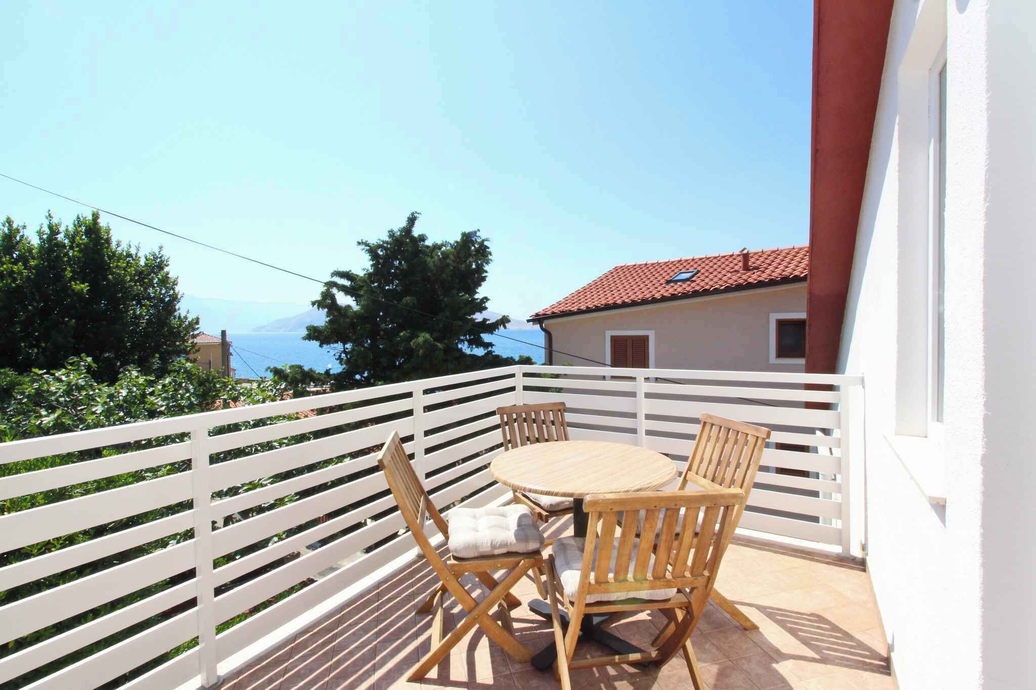 Un balcon avec une balustrade blanche, une table ronde en bois et quatre chaises en bois.