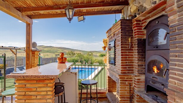 Eine Terrasse mit Backofen, Barhocker und Blick auf einen Pool.