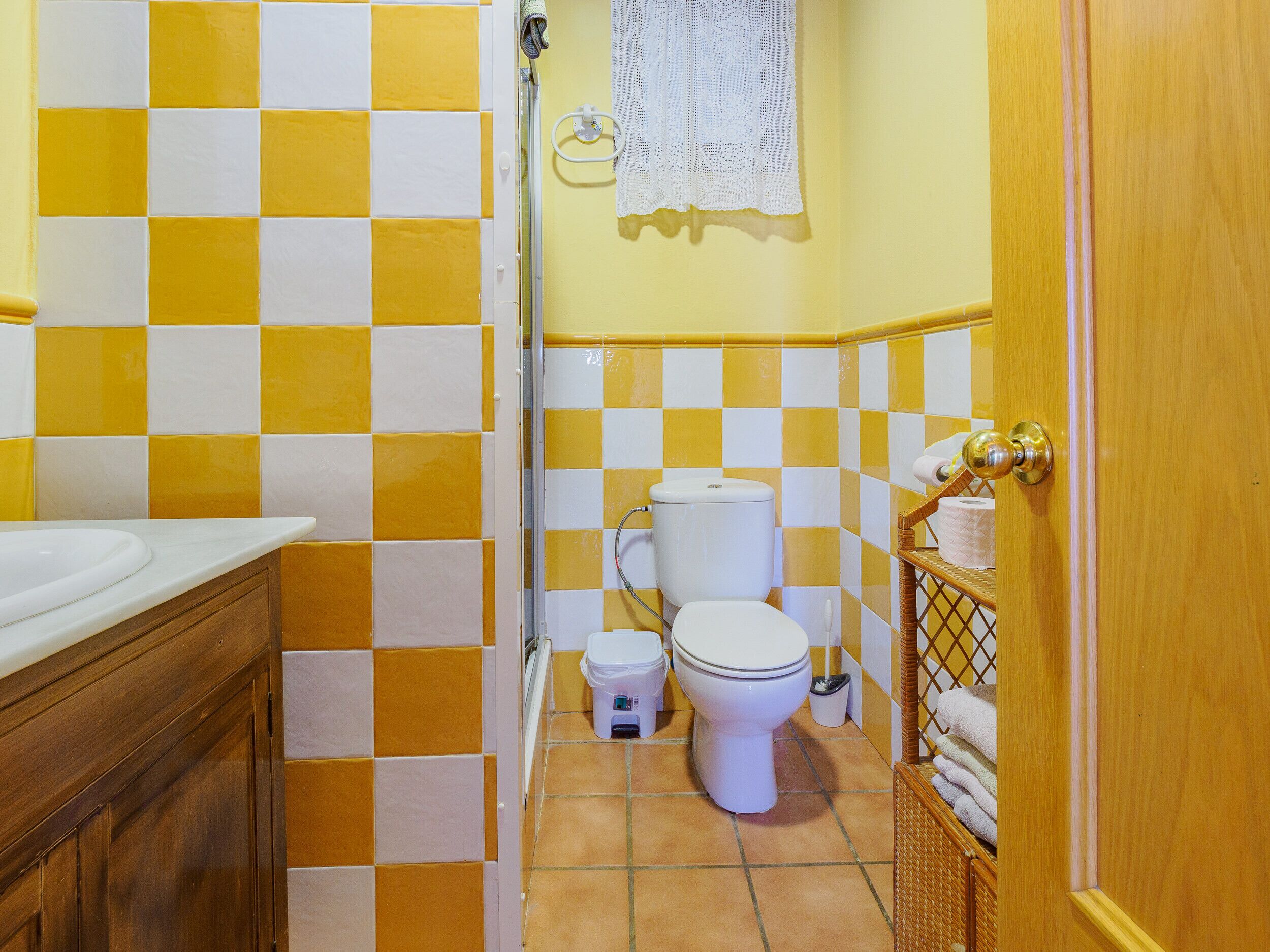 A bathroom with yellow and white checkered tiles, a white sink, a toilet, and a wicker basket with towels.