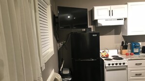 A compact kitchen with a black refrigerator, a stove, and white cabinets.