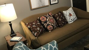 A living room with a brown sofa, patterned pillows, a framed picture of a llama, and a lamp on a side table.