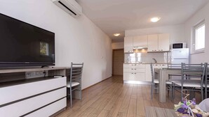 A modern kitchen with white cabinets, a flat-screen TV, and a dining area with a table and chairs.
