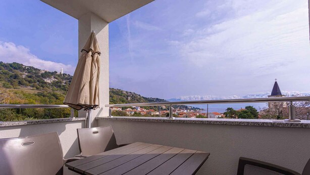 A balcony with a table and chairs, overlooking a scenic view of a hill with buildings and a church.
