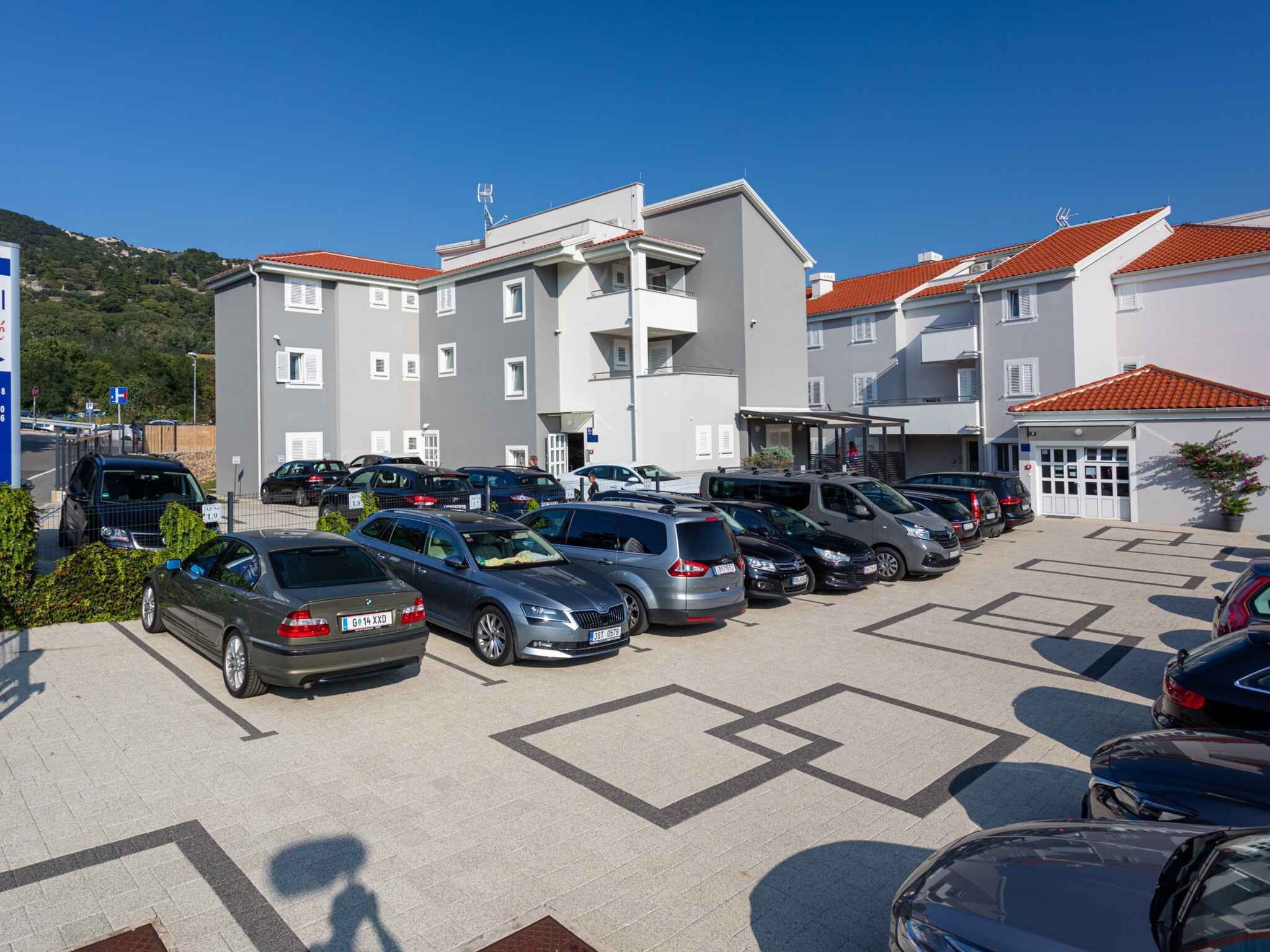 Un parking rempli de voitures, un bâtiment avec un toit rouge et un paysage montagneux en arrière-plan.