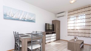 Una sala de estar moderna con una mesa de comedor, sillas, un televisor, un mueble y una pequeña mesita.
