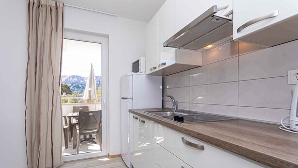 Una cocina moderna con armarios blancos, un lavamanos de acero inoxidable y una ventana con vista a un balcón.