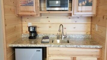 A compact kitchen with wooden cabinets, a microwave, a coffee maker, and a refrigerator.