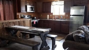 Una cocina con armarios de madera, un refrigerador de acero inoxidable, un microondas y una mesa de madera con bancos.