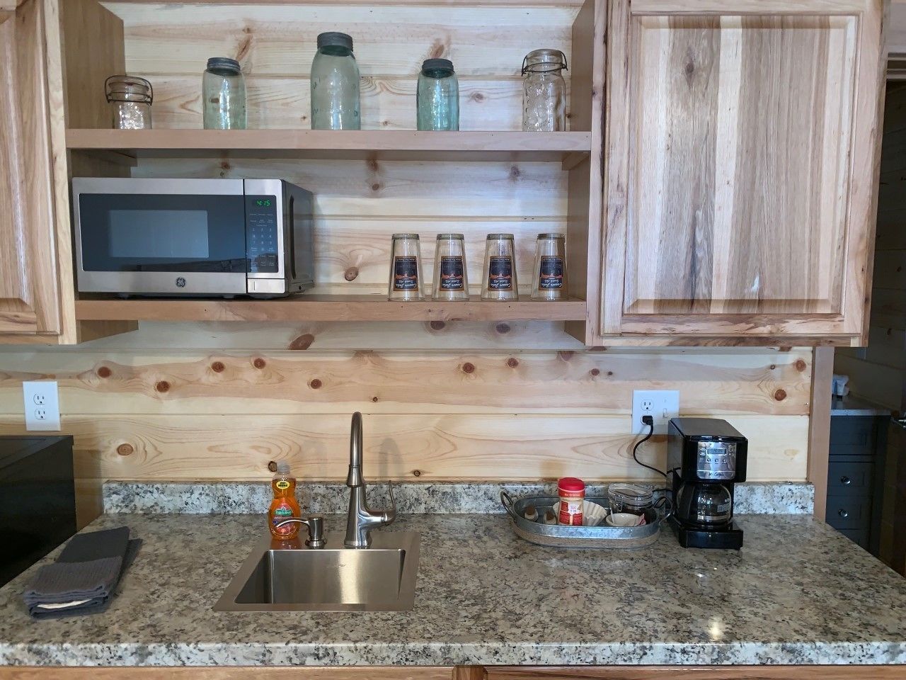 A kitchen with a granite countertop, stainless steel sink, a microwave, and wooden cabinets.