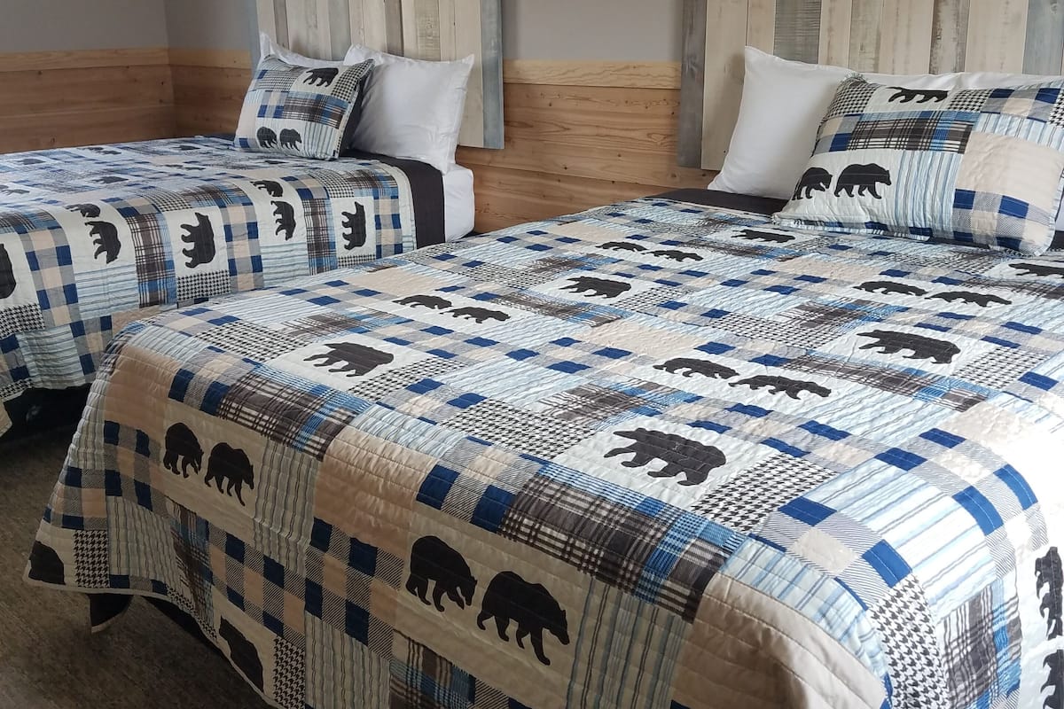 A hotel room with two beds, each with a quilted bedspread featuring animal patterns. The room has wooden headboards and a neutral color scheme.