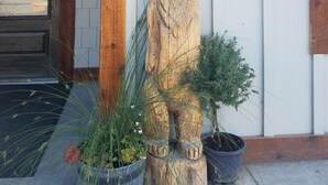 A wooden bear statue on a porch with a lantern above it, surrounded by potted plants. - 406 Lodge (Gardiner)