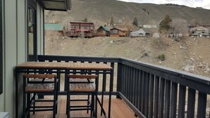 A wooden deck with a table and chairs, overlooking a rural landscape with houses and hills. - 406 Lodge (Gardiner)