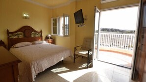 A bedroom with a bed, a chair, a TV, and a balcony with a view.