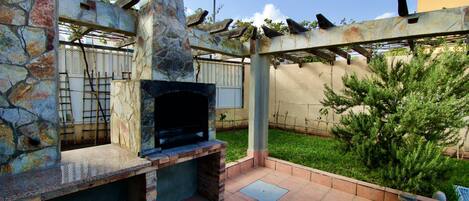Un patio exterior con chimenea de piedra, una pérgola con plantas trepadoras y un césped bien cuidado.