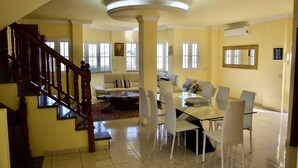 A spacious living area with a dining table, chairs, a sofa, and a staircase.