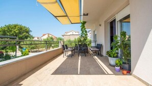 Ein Balkon mit gelbem Sonnenschirm, Sitzgelegenheit im Freien und Blumentöpfen.