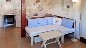 A cozy room with a white sofa, a small table, a kitchen area with a stove, and a dining table. - Holiday apartment mit Terrasse (Baška)