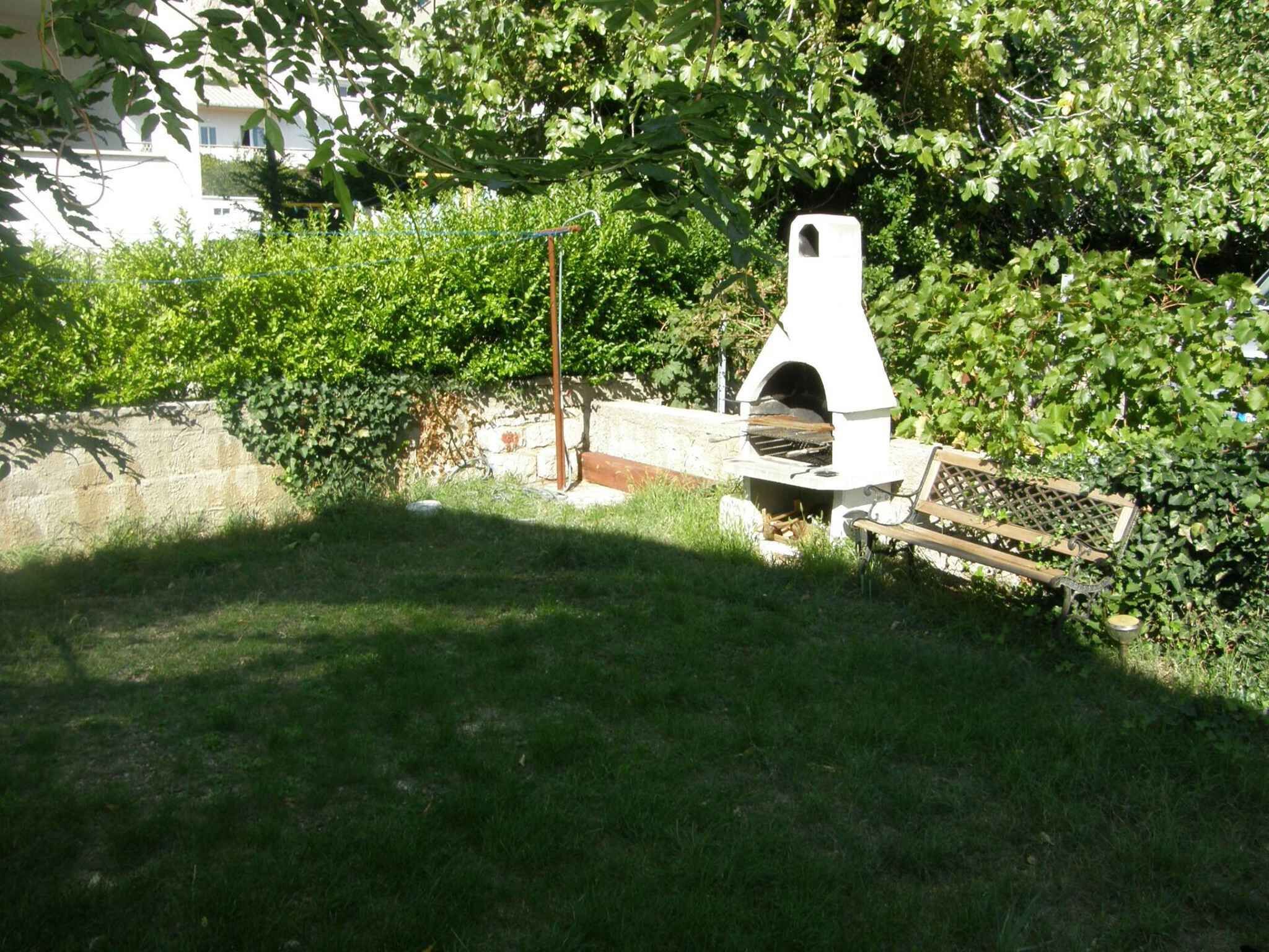 A white outdoor grill with a chimney, surrounded by greenery and a stone wall.