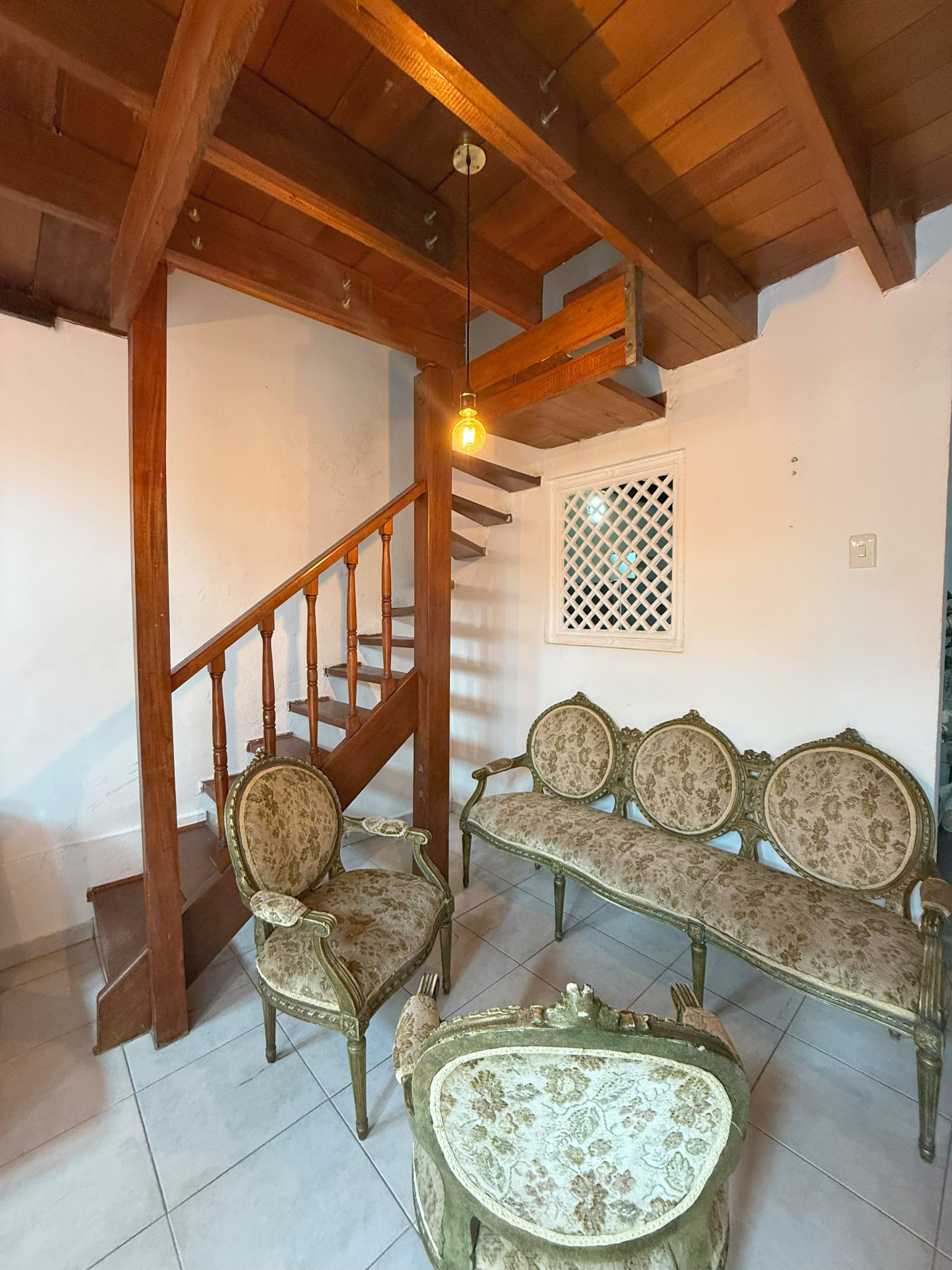 A room with a wooden staircase, a bench, two chairs, and a small table.