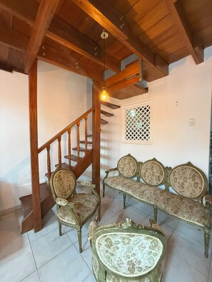 A room with a wooden staircase, a bench, two chairs, and a small table.