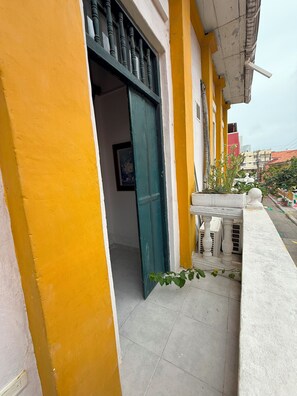 Un bâtiment jaune avec une porte verte, une balustrade blanche et un sol carrelé.