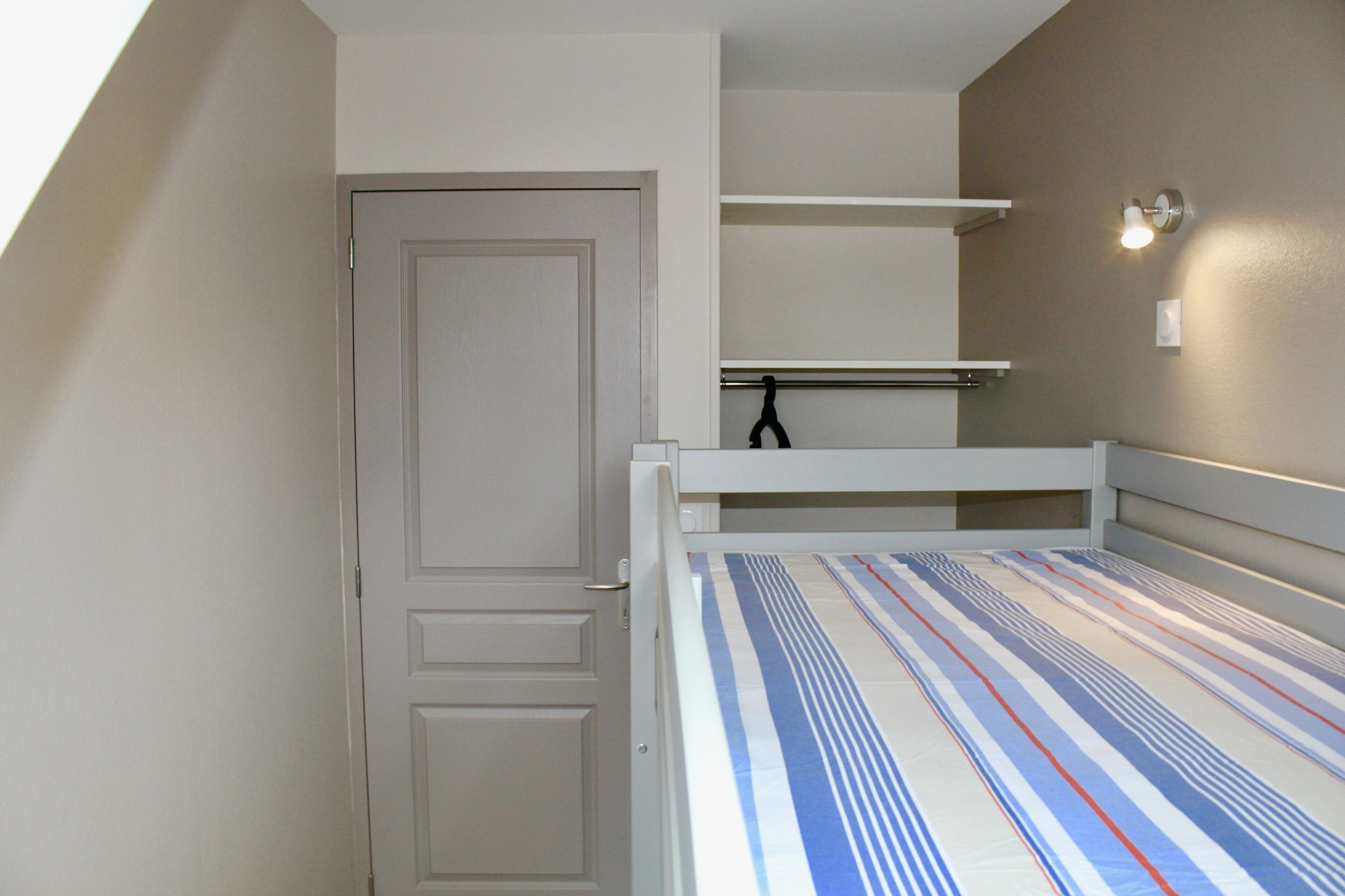 A bedroom with a bed, a door, and a shelf unit against the wall.